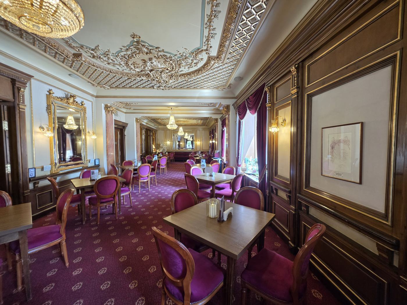 Salonul Casei Capșa din București, cu tavan din stucatură aurită, candelabre de cristal și mobilier tapițat în purpuriu