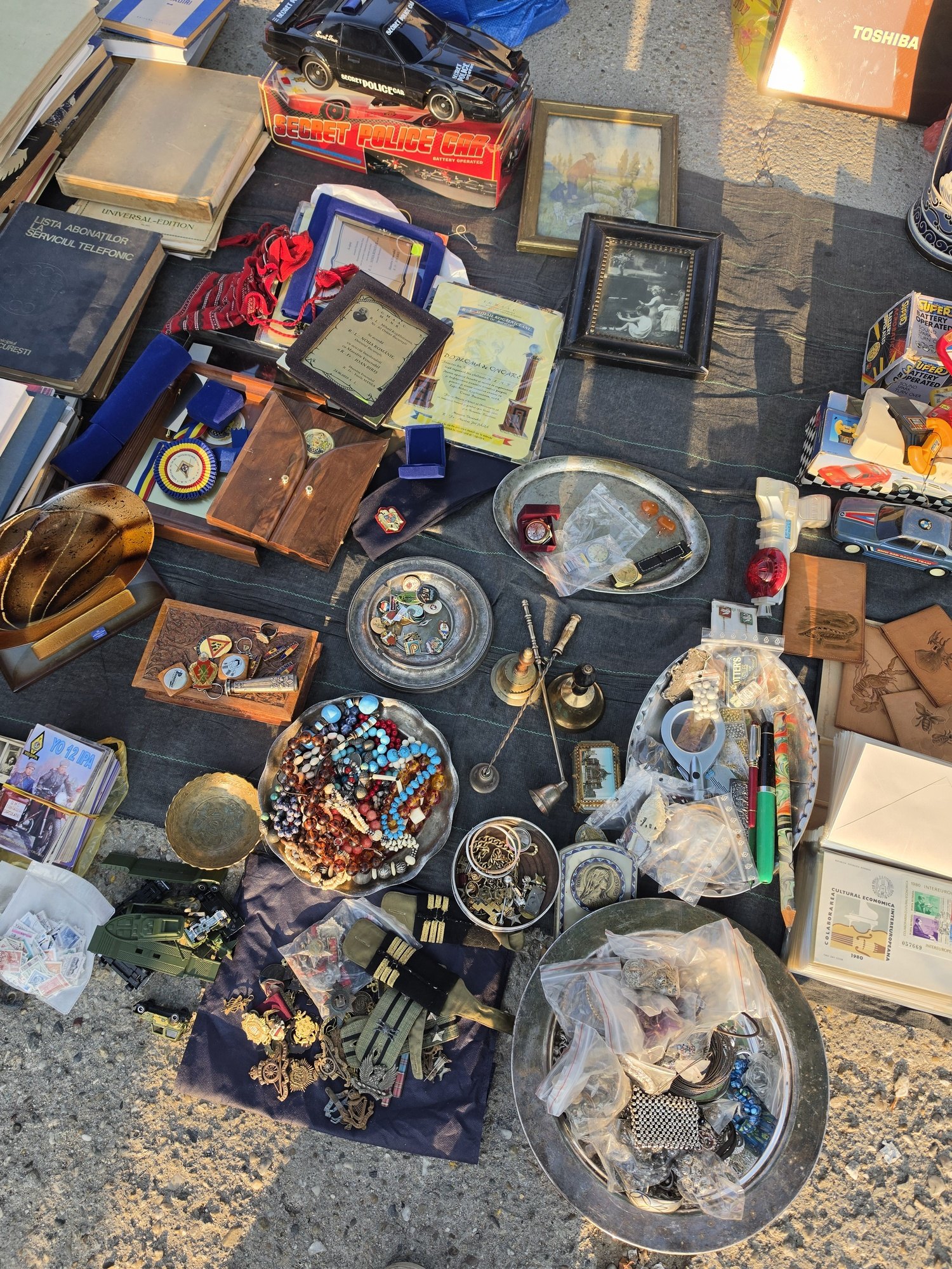 Books, framed pictures, diplomas, badges, medals, military insignia, beads, brassware and stamps laid out on a cloth at the Bucharest flea market