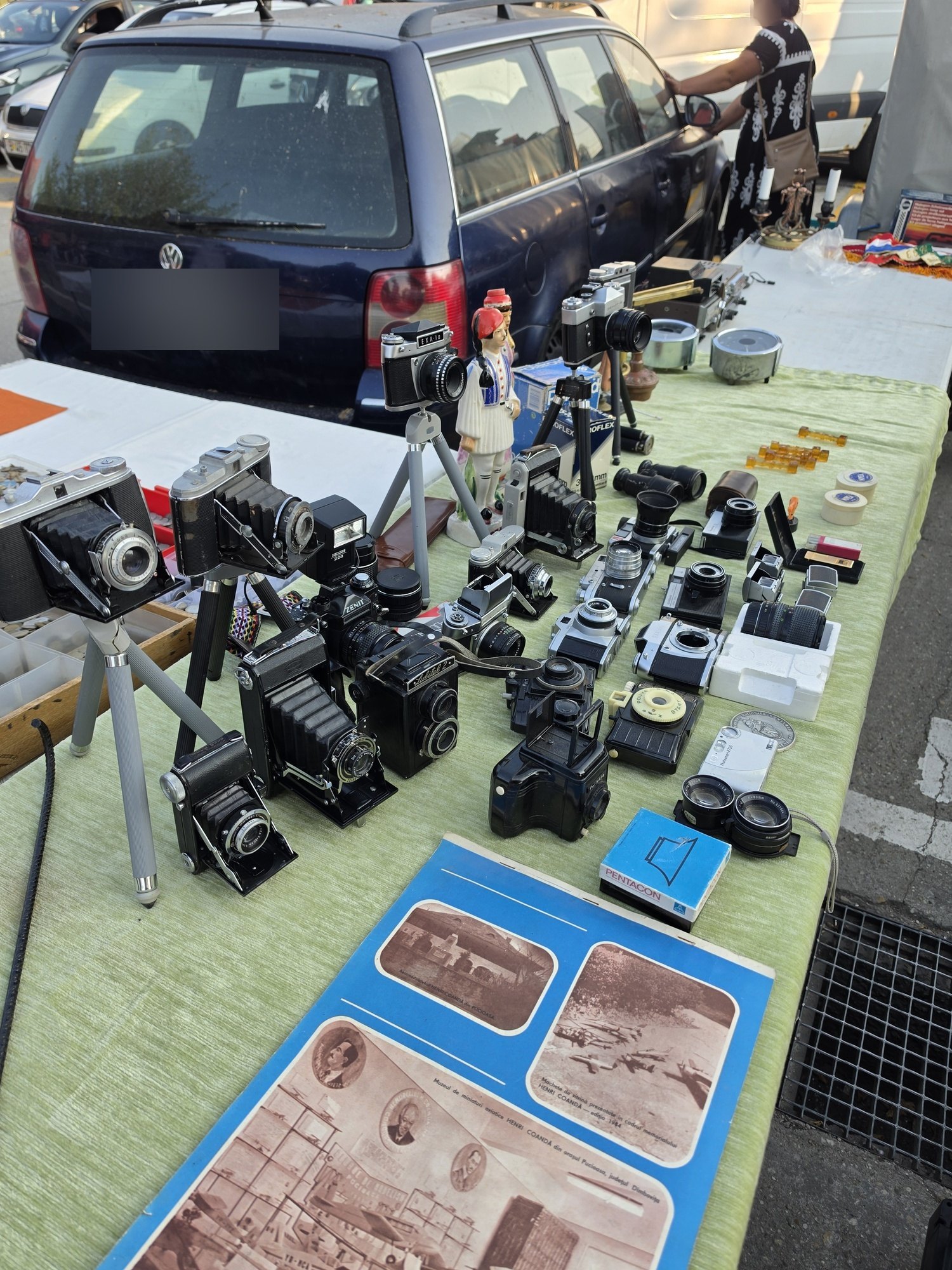 A table of vintage film cameras, folding cameras, lenses and tripods at the Valea Cascadelor flea market