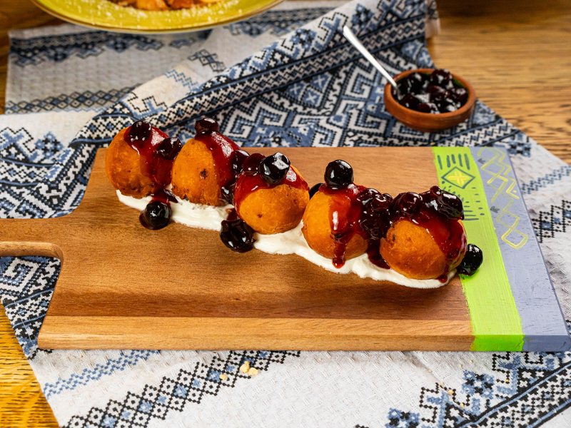 Papanași served as balls on sour cream with sour cherry jam, on a wooden board at Restaurant Ceaun